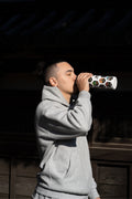 Person in gray hoodie drinking from a colorful cup against a dark background drinking out of the cheku Japane Destinations Traveler Bottle