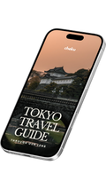 Phone displaying a Tokyo travel guide app with a scenic background of Imperial Palace and text that says cheku Tokyo travel guide through our lens